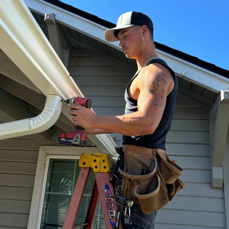 Gutter installer fastening a white downspout and elbow on a home in St. Helens, Oregon