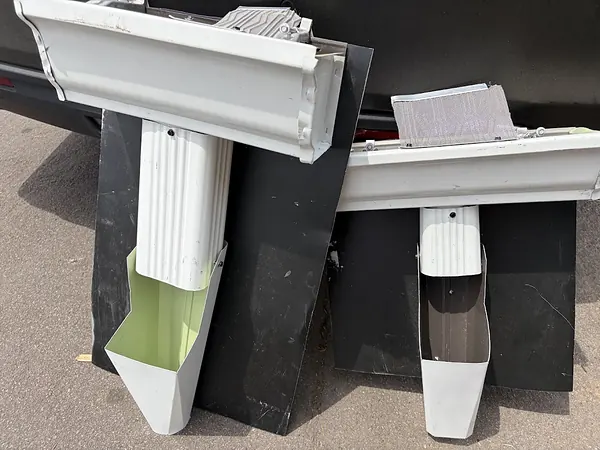 Side-by-side sample of a larger 3x4 downspout and outlet next to a smaller 2x3 downspout on white K-style gutter sections