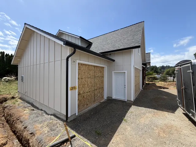 Black downspout at the corner of a garage under construction in Scappoose, next to an open trench