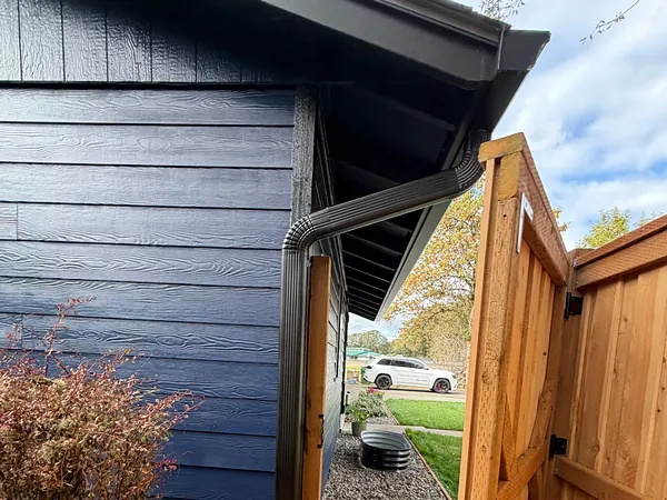 Black seamless gutter and downspout on navy lap siding next to a new cedar side gate in St. Helens