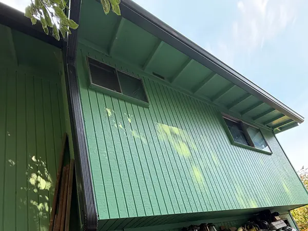 Dark seamless gutter and downspout on the tall green side of a split-level home in Oregon City