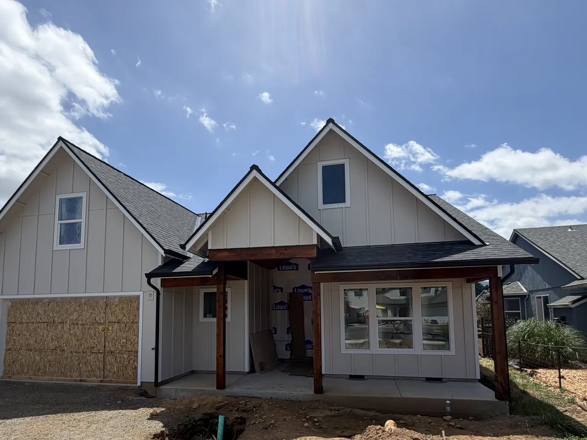 Board-and-batten home under construction in Scappoose with black gutters along the gables and porch roof and black downspouts at the corners