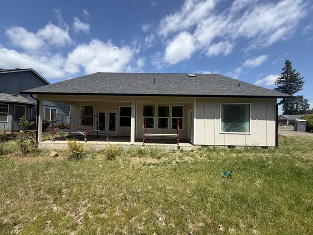 Rear of a single-story Scappoose home with black gutters along the hip roof and a covered patio