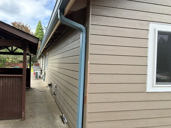 Blue seamless gutter and downspout running down the side of a tan lap-sided home beside a covered patio