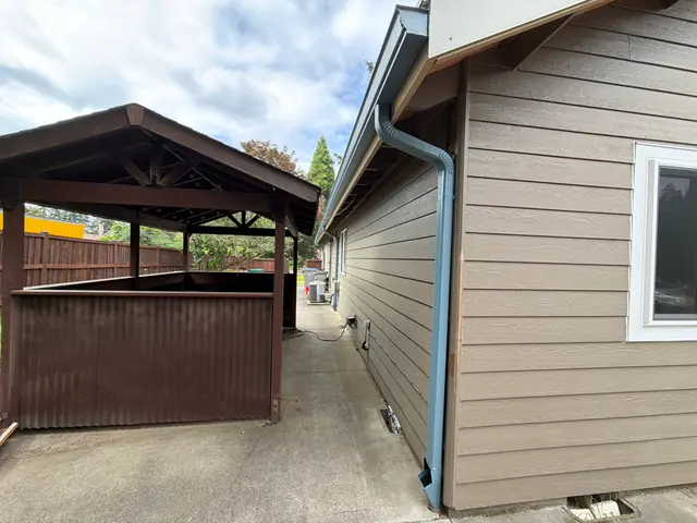 Blue-gray gutter and downspout on the tan siding of a Tigard home beside a covered carport