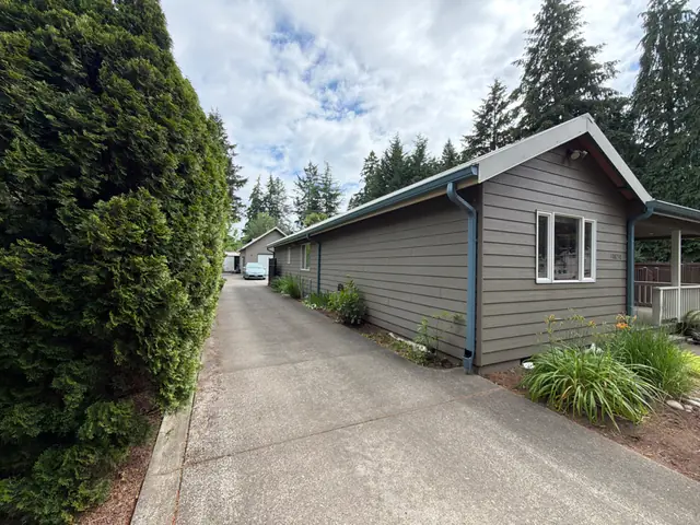 Long single-story tan home in Tigard with blue-gray gutters and downspouts along the driveway side