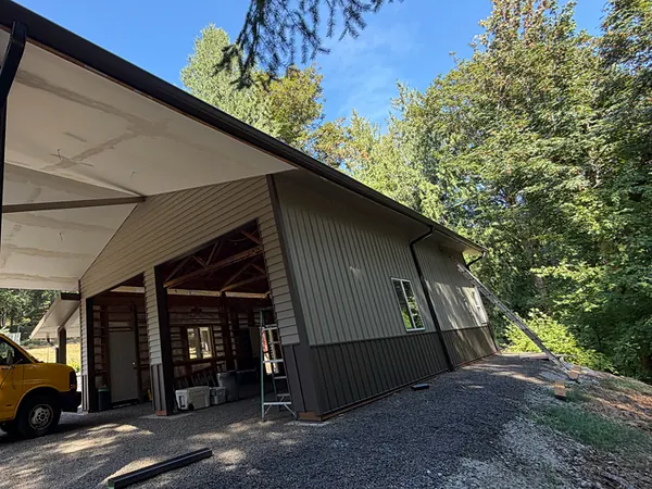 Dark brown gutter and downspout on a large shop building with a covered carport among fir trees near St. Helens
