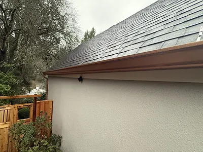 Copper-toned seamless gutter running along the eave of a white stucco Portland home