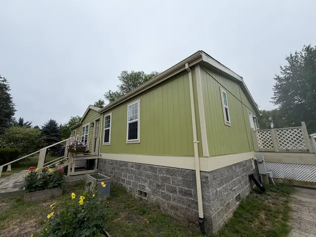 Green manufactured home in Vernonia with cream-colored gutters and downspouts along the side