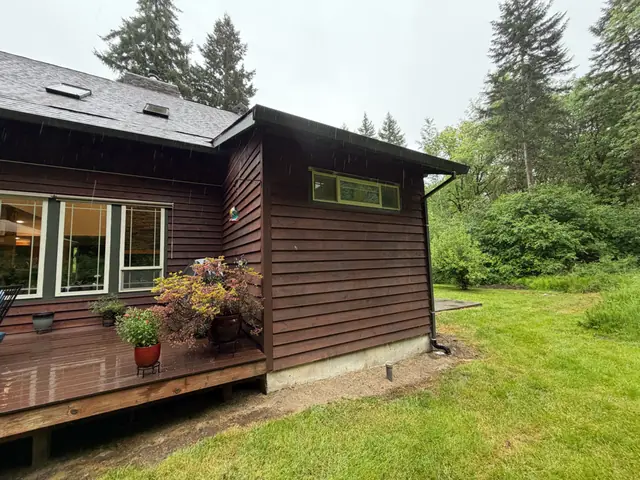 Brown cedar-sided home in Vernonia with dark gutters and a downspout at the corner beside a deck