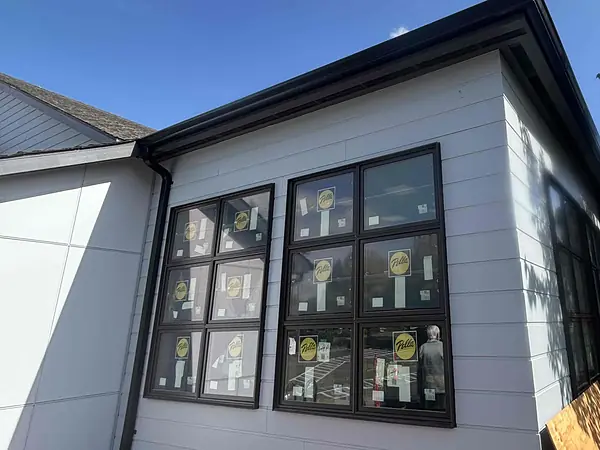 Dark seamless gutter and downspout on a light gray community building in Wilsonville with black-framed windows