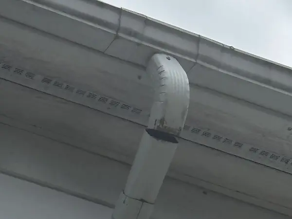 White downspout elbow separated from the downspout below the gutter outlet, leaving an open gap