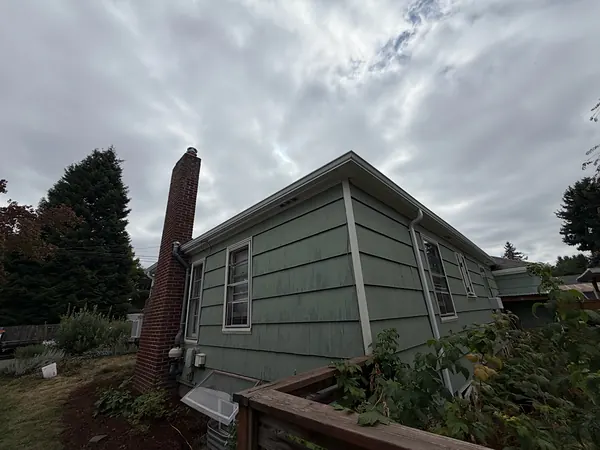 Green-sided Portland bungalow with a brick chimney and seamless gutters and downspout under a cloudy sky