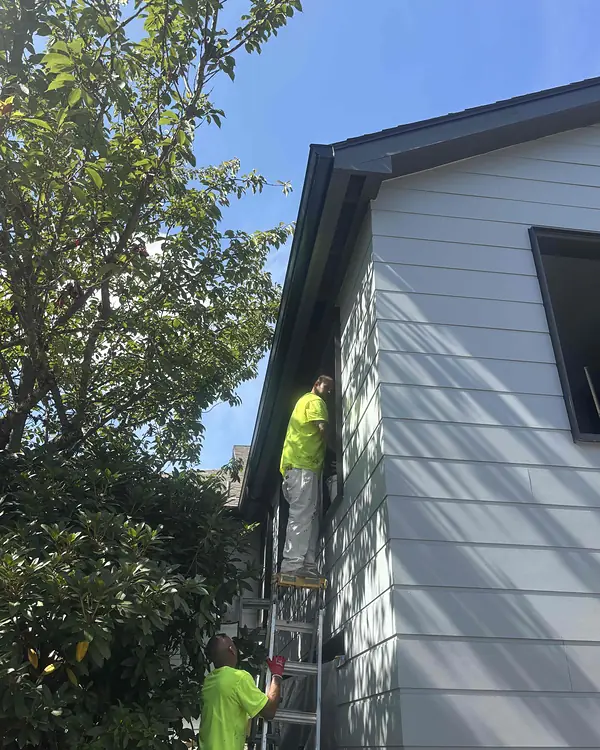 Two installers in hi-vis shirts on ladders at the corner of a gray community building in Wilsonville