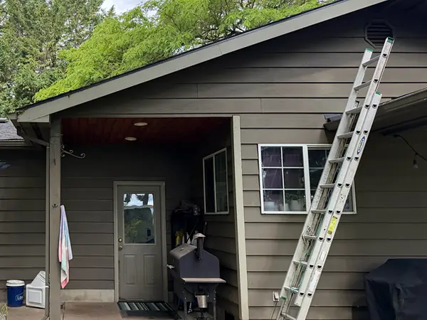 Ladder set against the eave of a brown Hillsboro home during a gutter installation, next to a covered back patio