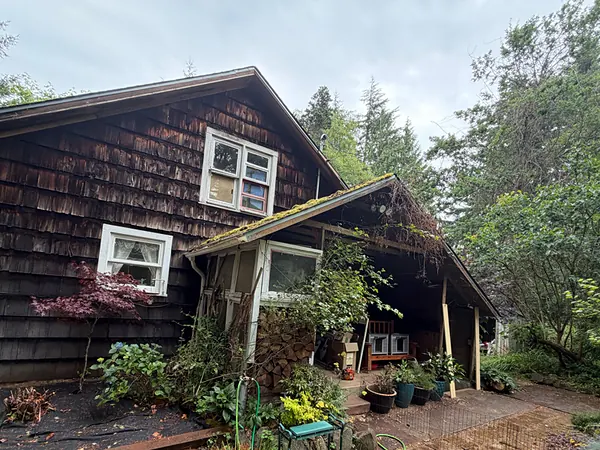 Cedar-shake Clatskanie home with a covered porch and garden, tucked under tall fir trees