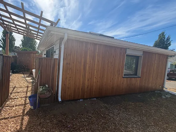 Cedar-sided backyard ADU in Portland with a white seamless gutter and downspout beside a wood pergola