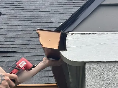 American Gutter Service installer fastening a copper-colored gutter corner to the fascia of a Portland home