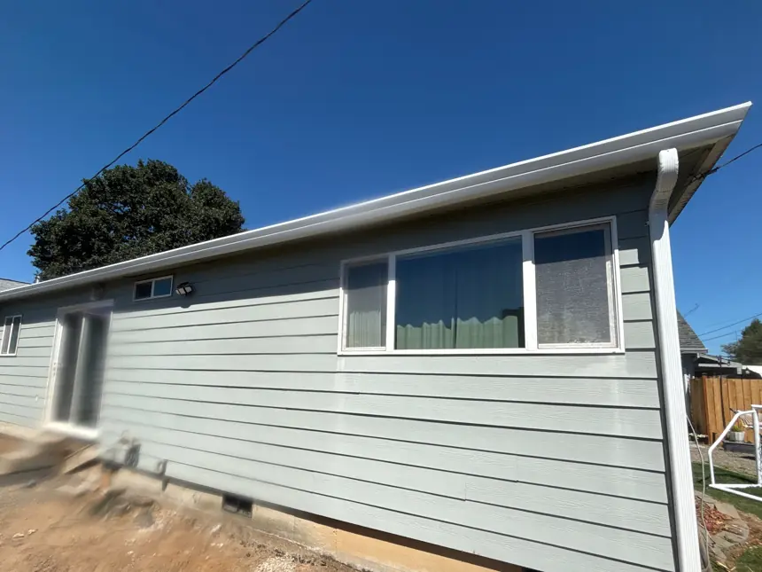 Sage-green ranch home in St. Helens with new white seamless gutters and a downspout at the corner
