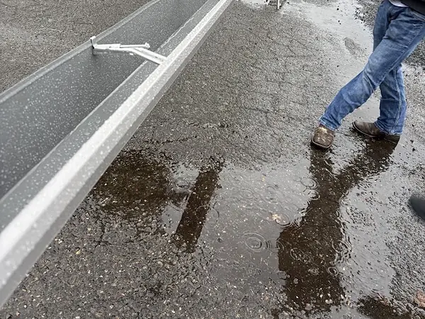 Freshly formed seamless aluminum gutter with hidden hangers laid out on a wet street in Columbia City, Oregon, before install