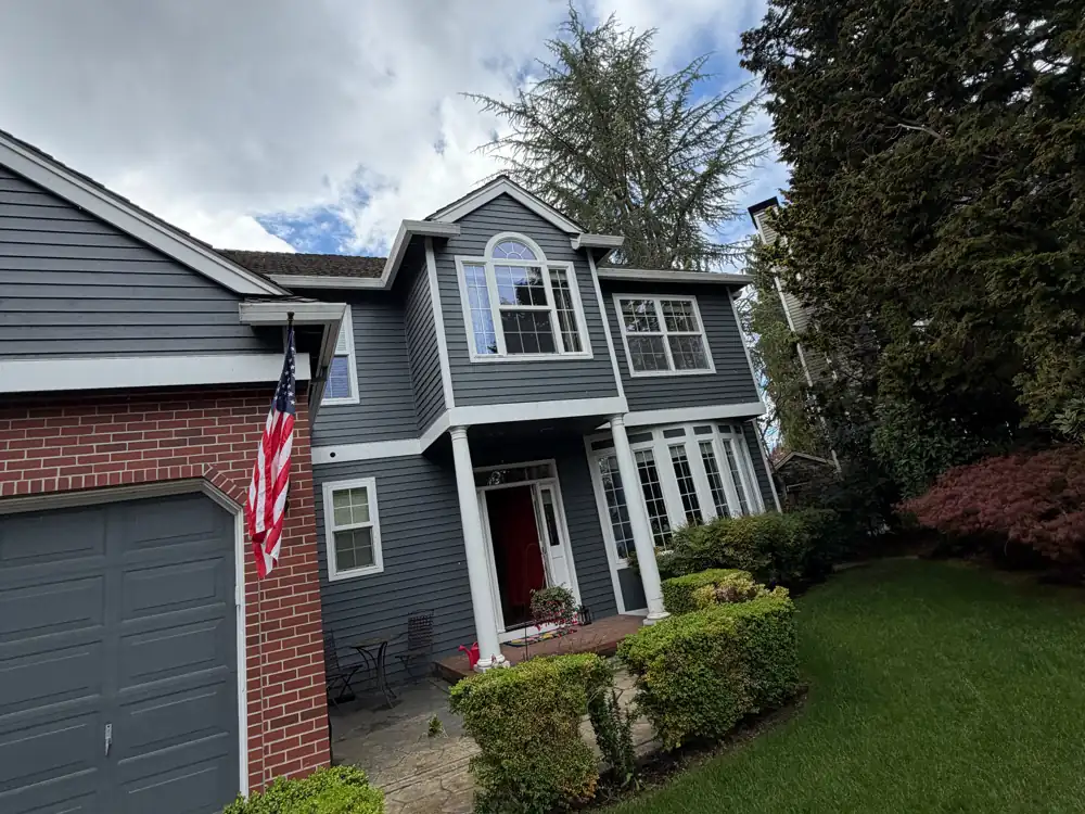 Blue two-story Oregon home with new white seamless gutters on every roofline, a red front door and a green front lawn