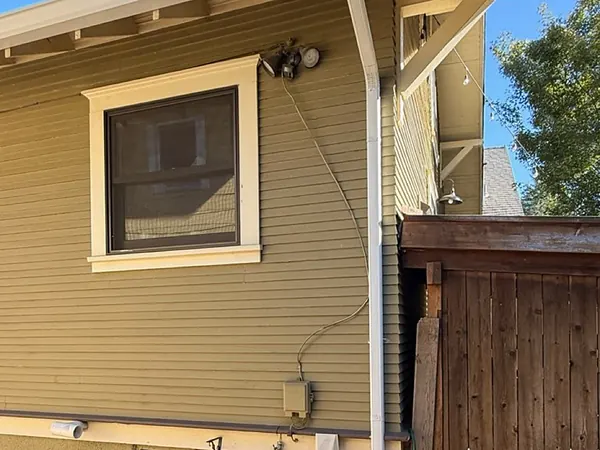 Olive-green Portland craftsman with a white seamless gutter and downspout beside a window and cedar gate