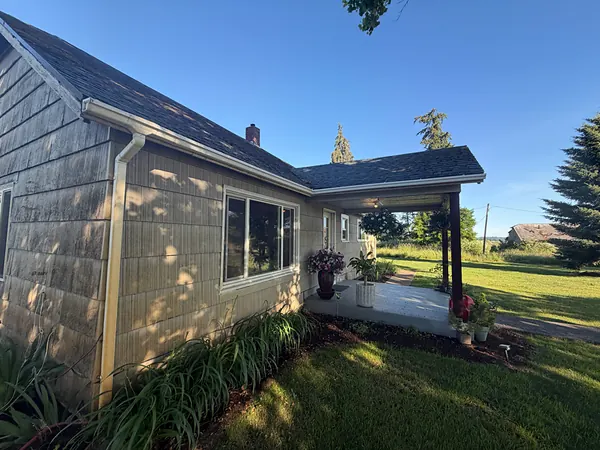 Shake-sided Scappoose ranch home with a white seamless gutter and downspout beside a covered side porch and open fields