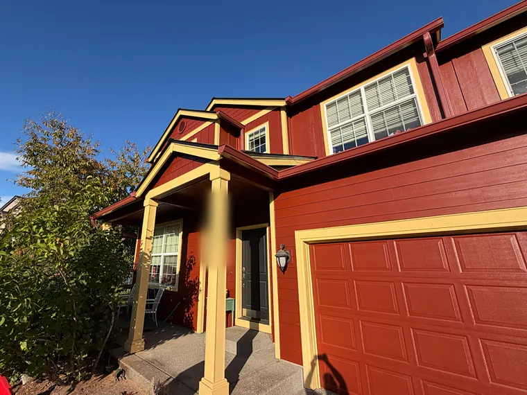 Red two-story Scappoose home with seamless gutters color-matched to the dark red trim above a covered porch and garage