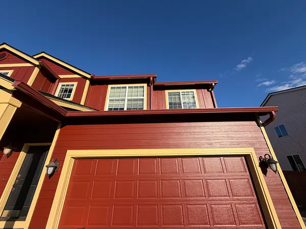 Red two-story Scappoose home with seamless gutters and a downspout that match the siding above the garage