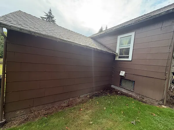 Seamless gutter wrapping an inside roof corner on a brown-sided Clatskanie home above a green lawn