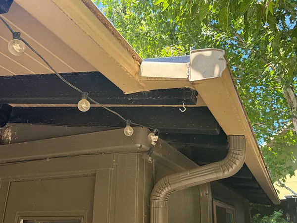 Close-up of a tan seamless gutter corner and outlet with a matching downspout elbow under a Portland porch roof