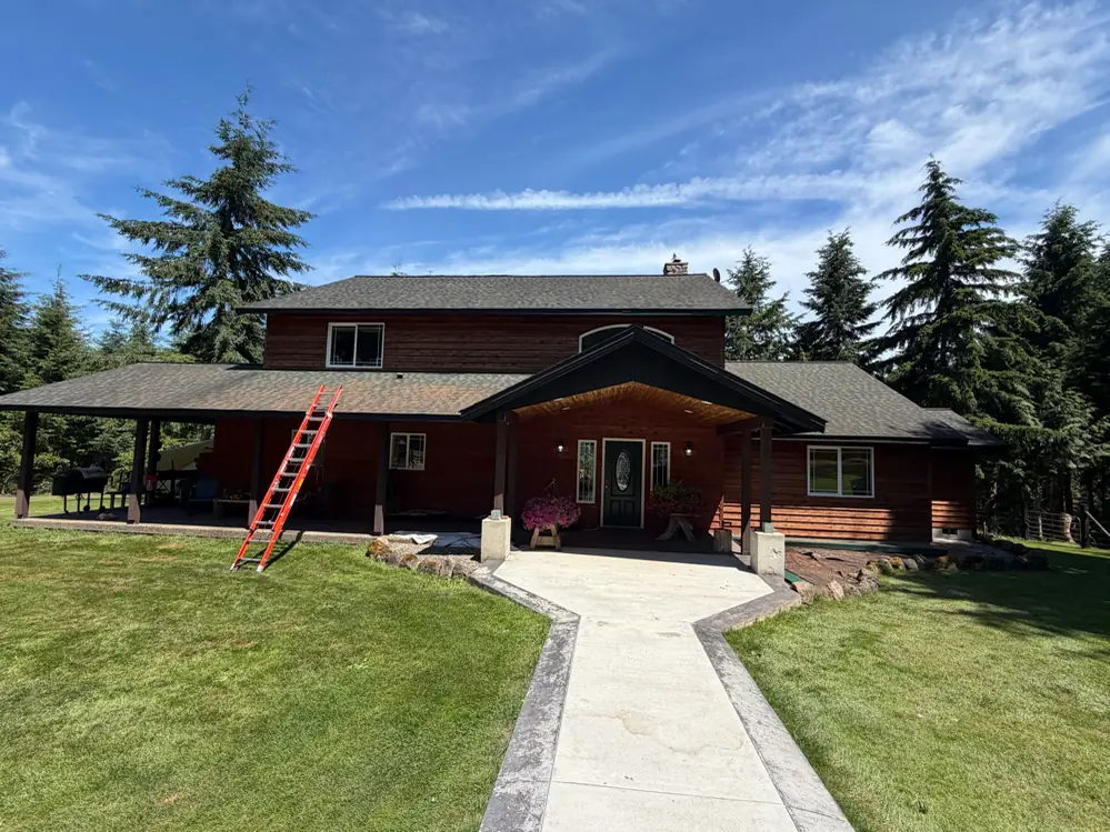 Two-story Clatskanie home with a wraparound covered porch and new seamless gutters, surrounded by tall Douglas firs