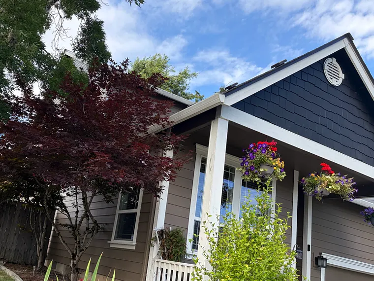 Navy and tan St. Helens home with white seamless gutters over a covered front porch with hanging flower baskets and a red Japanese maple
