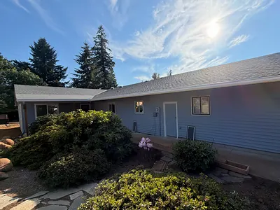 Back of the same Oregon City ranch with white seamless gutters along the eave and firs behind