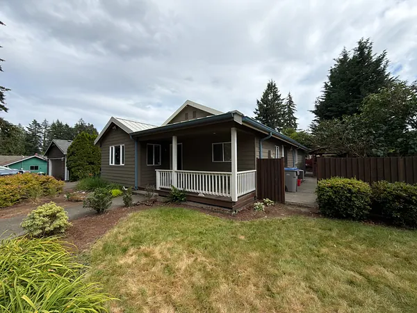 Ranch home with a covered front porch and seamless gutters, set among tall Douglas fir trees