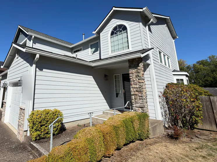 White gutters and downspouts along the lower and upper roof edges of a gray two-story house with a stone entry column