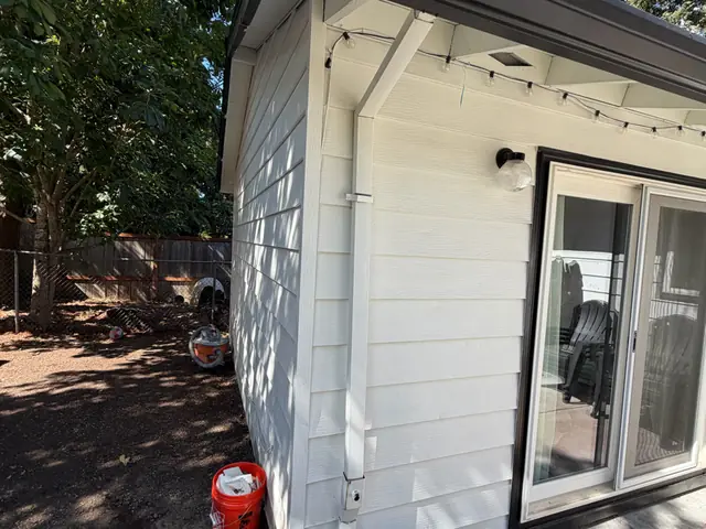 White downspout at the corner of a small white backyard building with a dark gutter in Beaverton