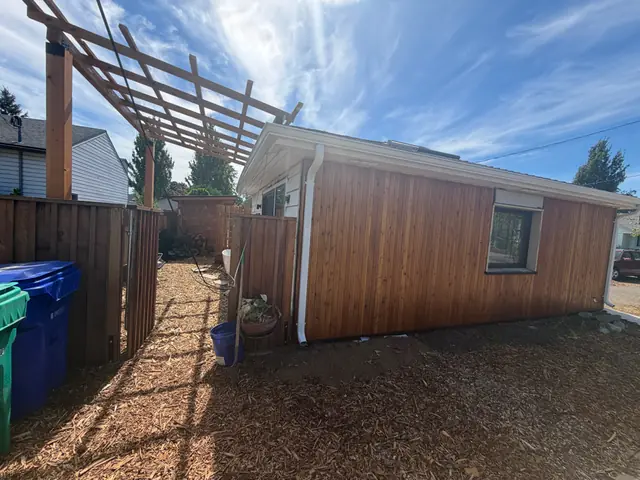 White downspout on a cedar-sided backyard building in Portland beside a wood pergola