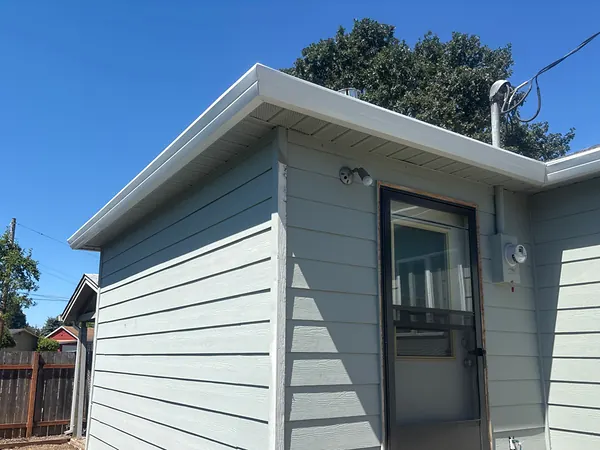 White seamless gutter wrapping the corner of a light blue home with a white downspout running down the wall