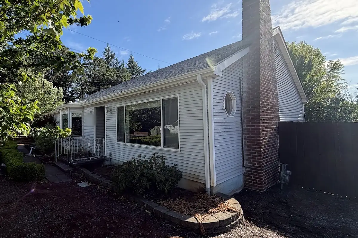 Single-story Oregon ranch home with a new white downspout running down the corner beside a brick chimney