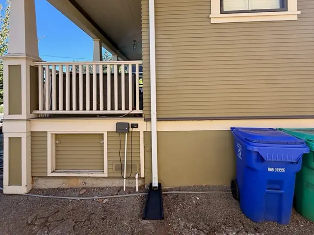 White downspout with a black splash block beside the porch of a tan craftsman-style home in Portland