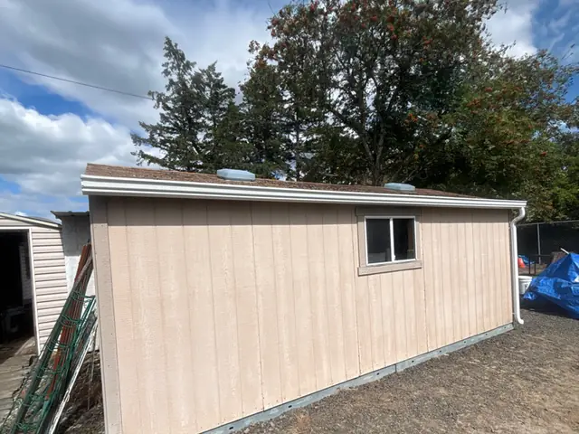 Tan detached shed in a Beaverton backyard with a white gutter along its roof edge
