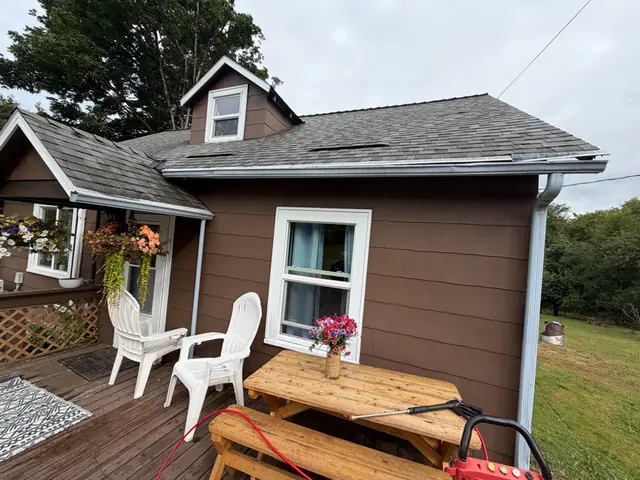 Brown-sided home in Clatskanie with a white gutter along the eave and a white downspout beside the deck