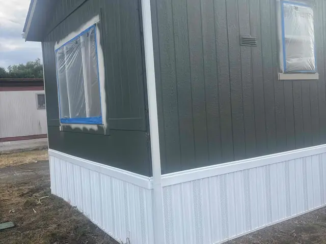 White gutter and corner downspout on a green-sided home with white metal skirting in Cornelius