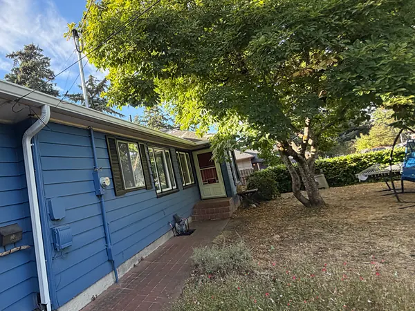 Blue Portland ranch home with white seamless gutters and a white downspout beside a shade tree