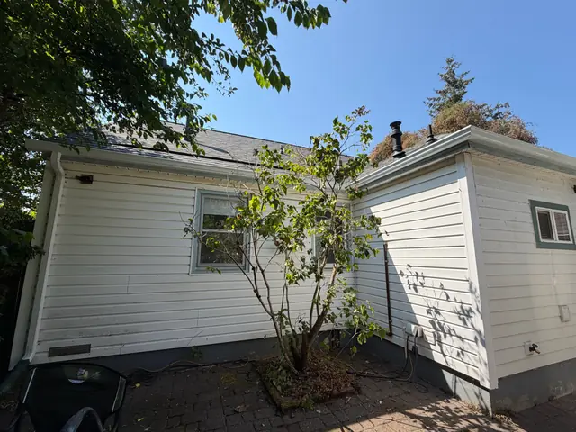 White gutters along the rear roof edges of a white-sided Portland home with a brick patio