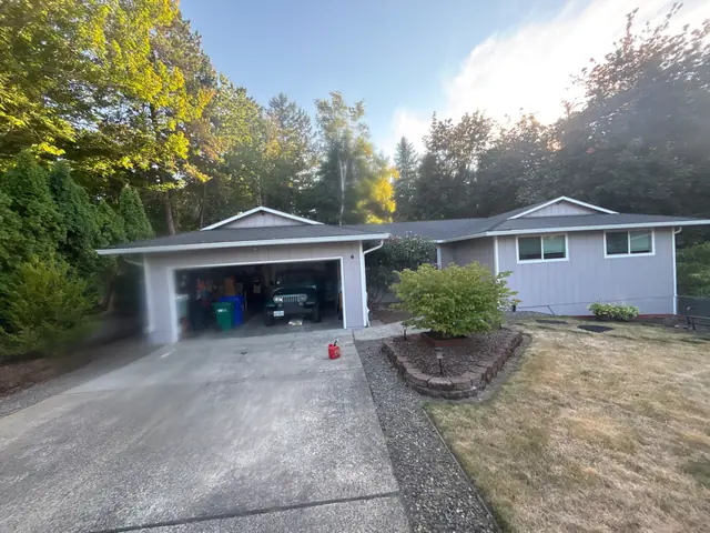 Single-story gray home in Gresham with white gutters along the garage and main roof, surrounded by tall trees