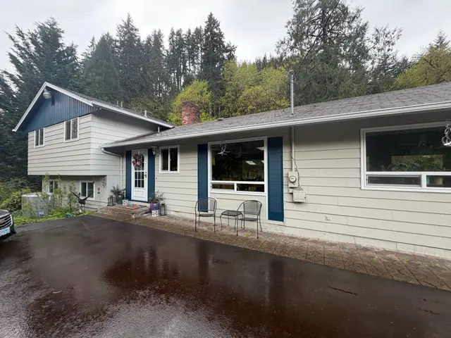 Split-level home in Scappoose with white gutters along both roof levels and a wet driveway in front