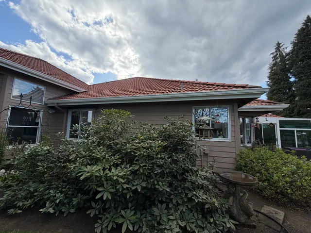 Warren home with a red tile roof and a white gutter along the eave above a large rhododendron