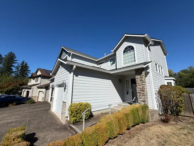 Two-story light gray home in Tigard with white gutters along several roof lines and a downspout beside the garage